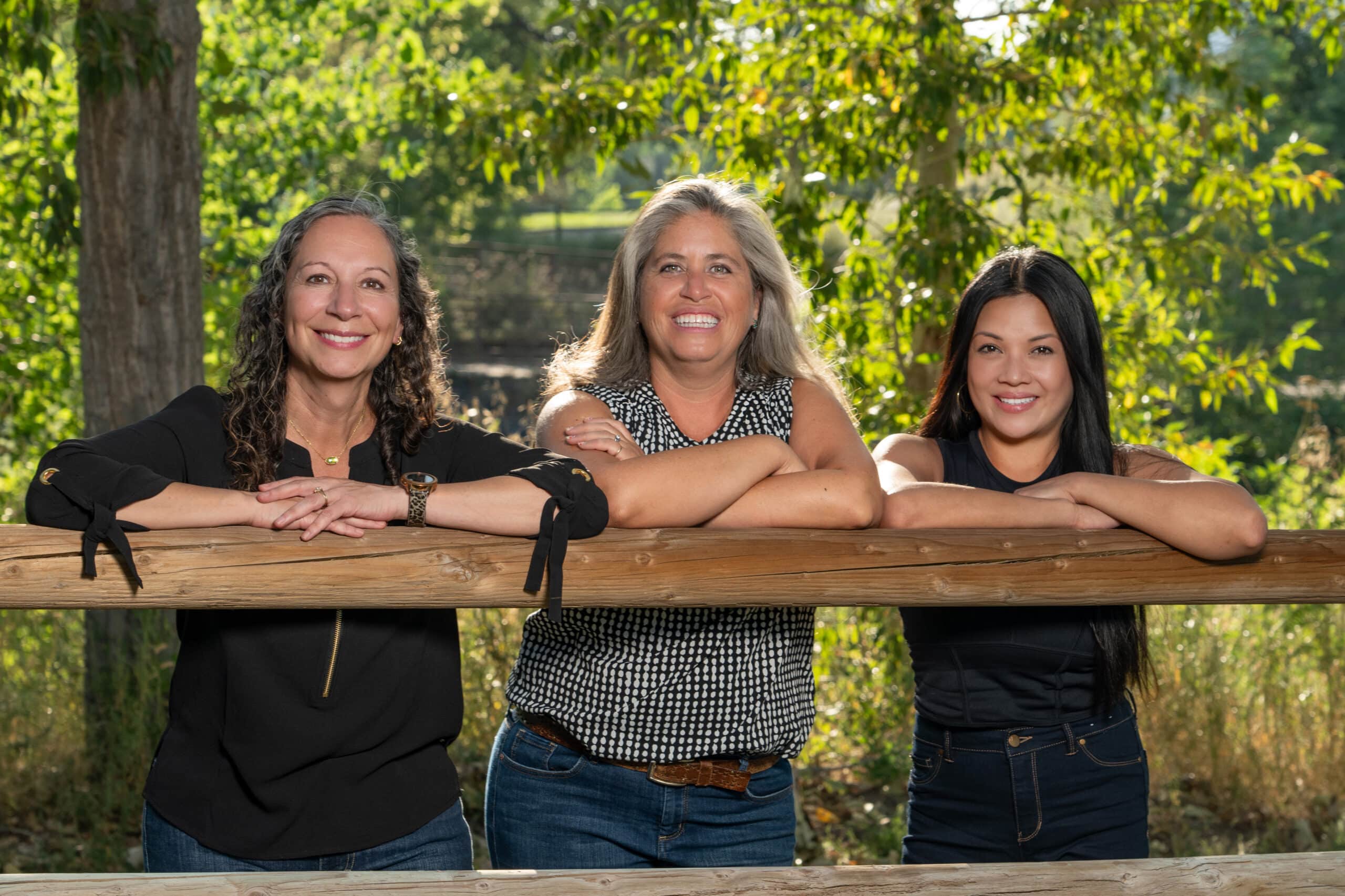 Three women leaning against wooden fence - Team behind Elmwood Dental in Littleton